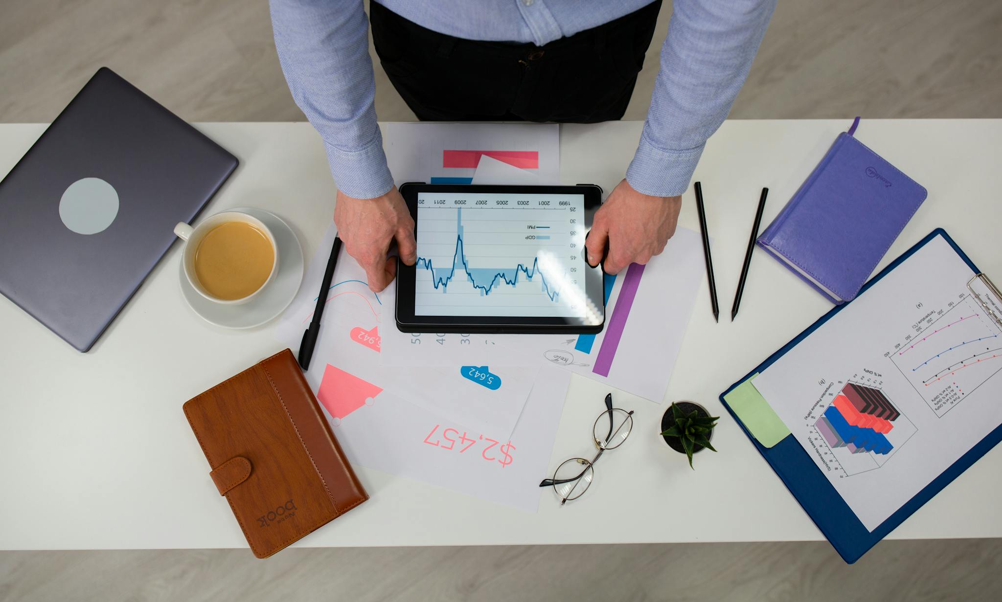 Overhead view of businessman using tablet to review data charts at a modern office desk.